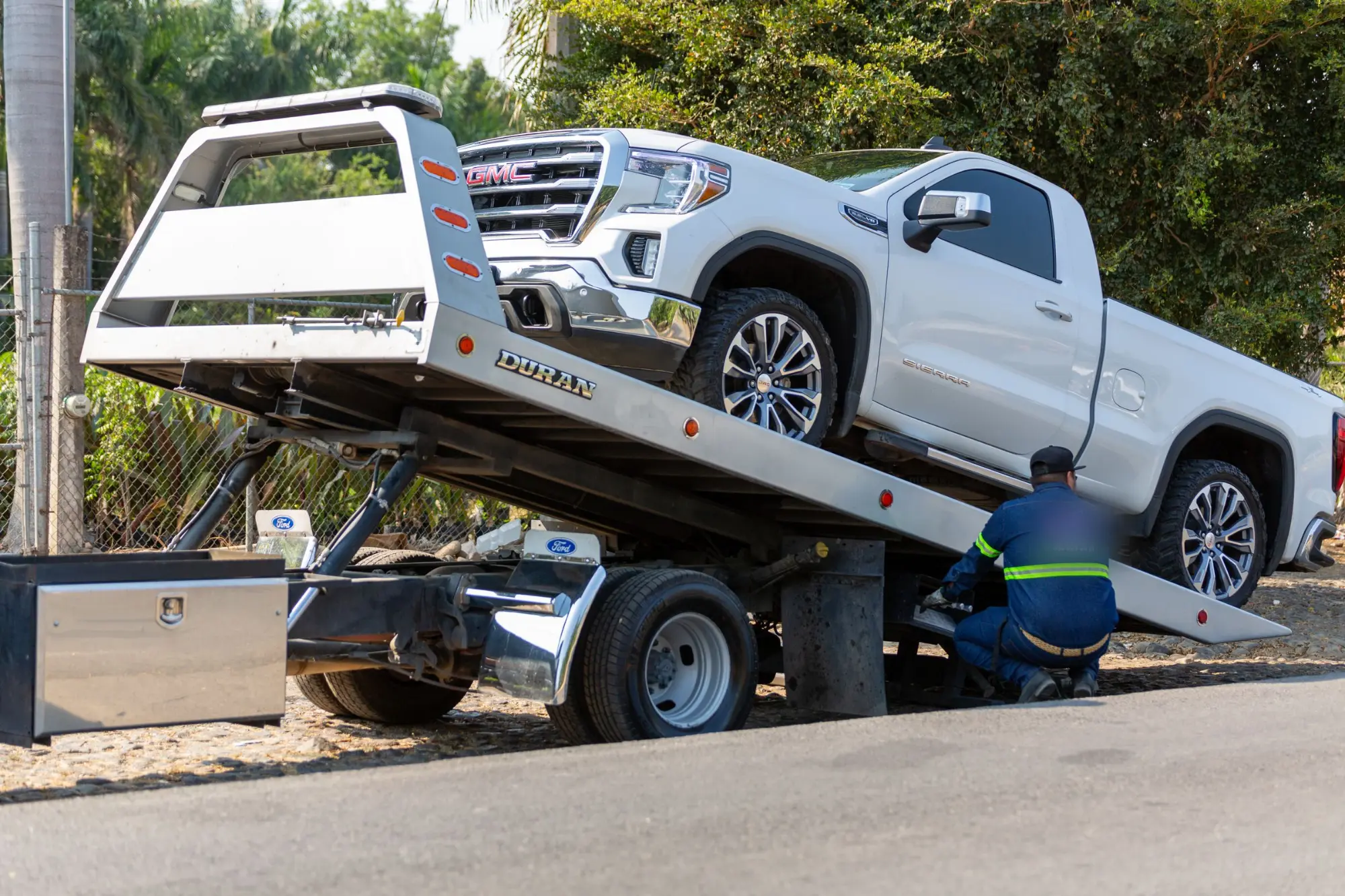 Flatbed tow truck loading a white pickup truck at the roadside